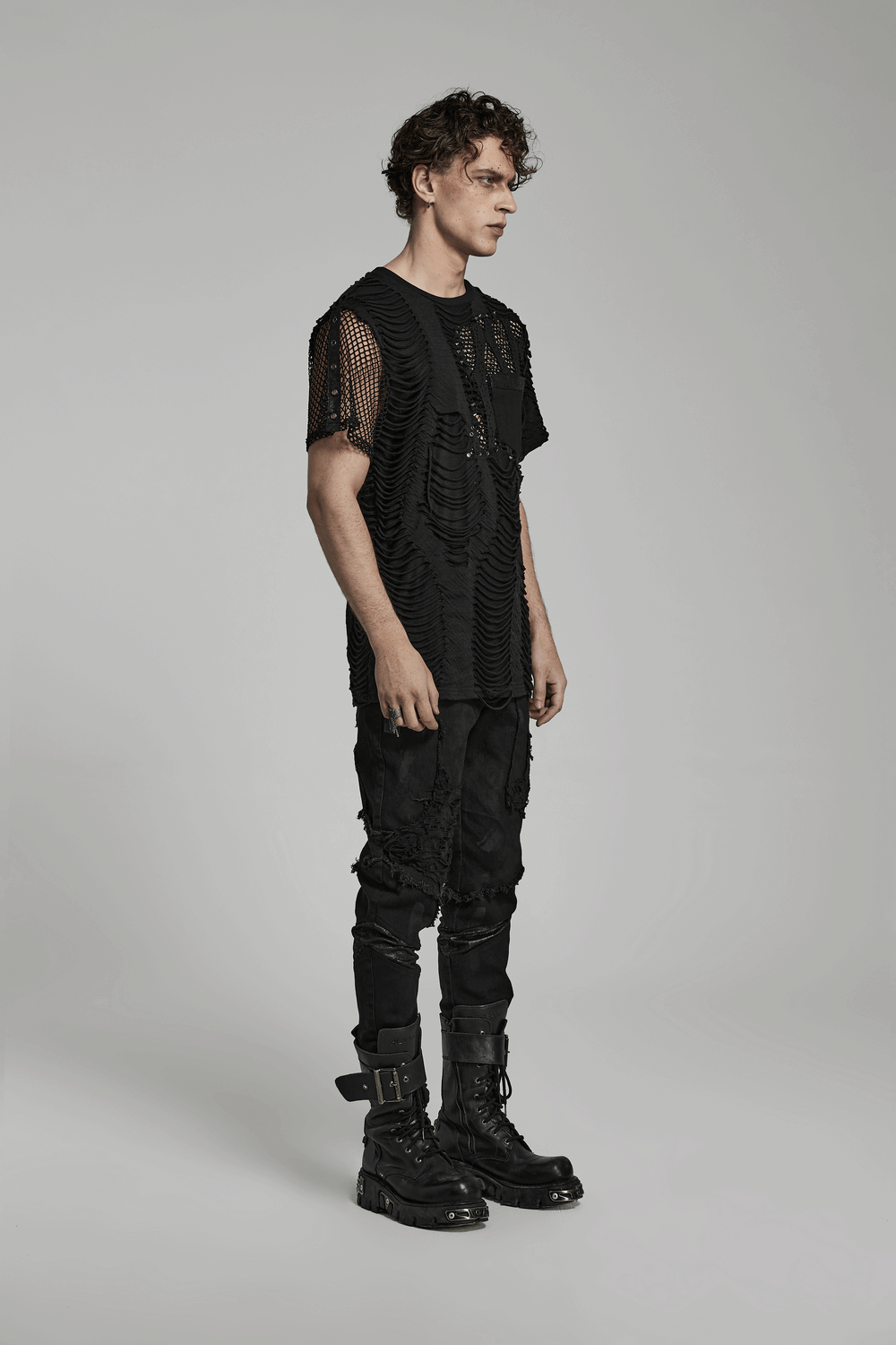 Edgy man in eyelet-studded black punk T-shirt with mesh splice design, showcasing bold fashion style.