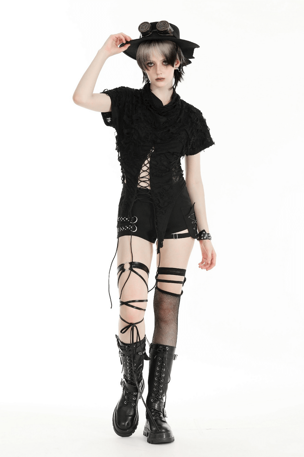 Model wearing a black asymmetrical ripped lace-up top, paired with shorts and chunky boots for an edgy look.