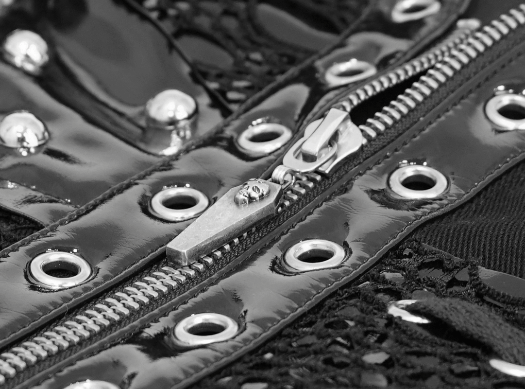 Close-up of a black punk style waistcoat zipper featuring silver rivets and eyelets for a gothic fashion look.
