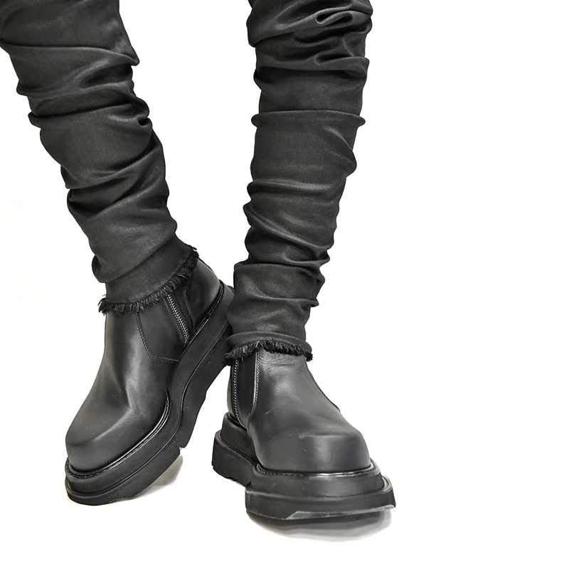 Men's black fashion boots with thick heel and side zipper, paired with stylish ruched pants for a modern casual look.
