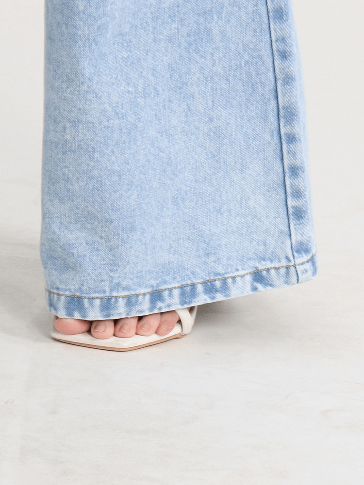 Close-up of wide-leg high waist denim pants with stylish footwear peeking out, highlighting casual chic fashion.