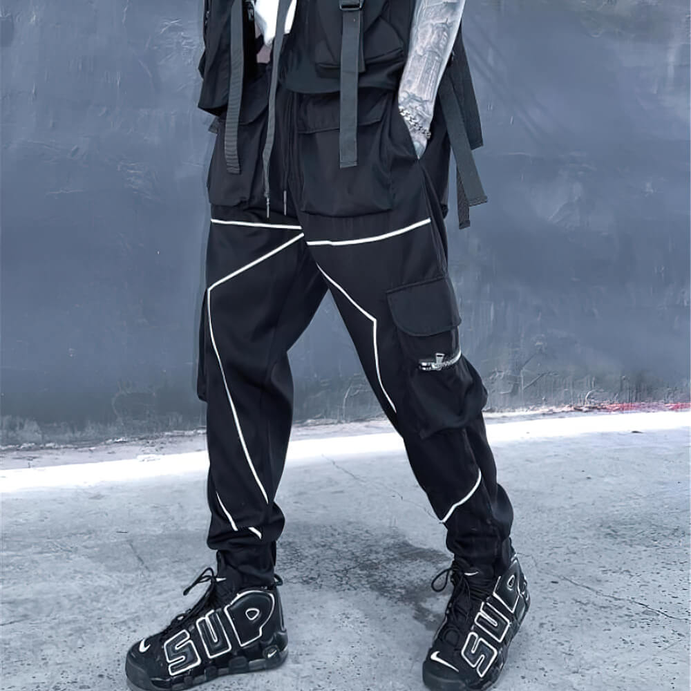 Men's black patchwork cargo trousers with elastic waist and pockets, styled with edgy sneakers.
