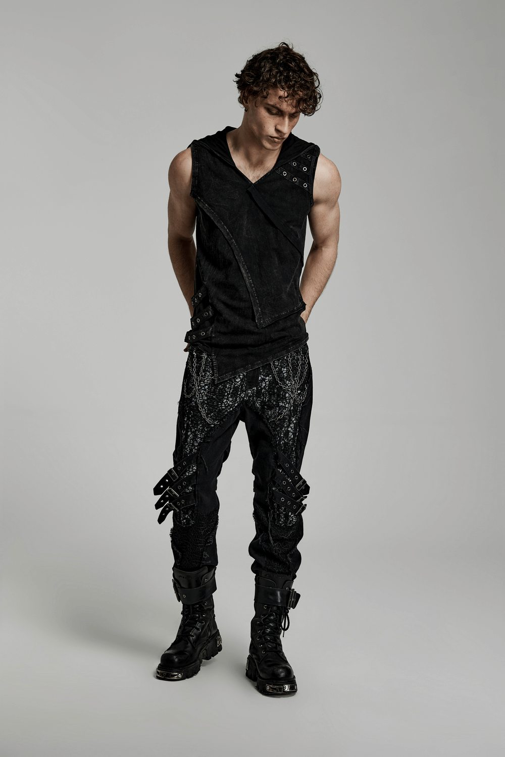 Stylish punk man in a black distressed hooded vest and edgy trousers, showcasing a unique rockstar look.