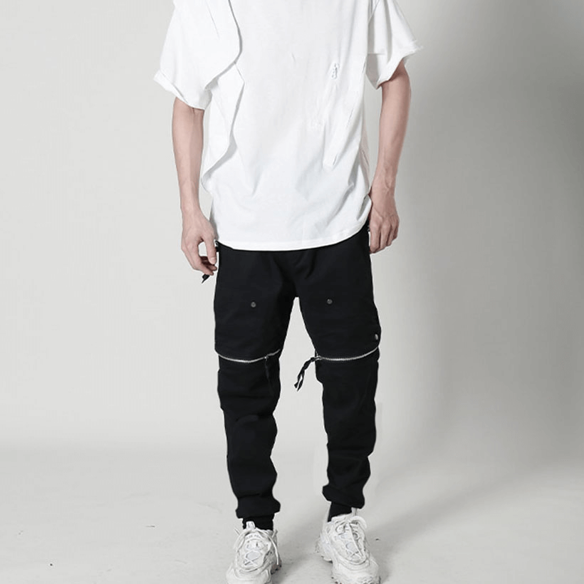 Stylish male model wearing black tactical zipper trousers and a loose white tee, showcasing edgy fashion.