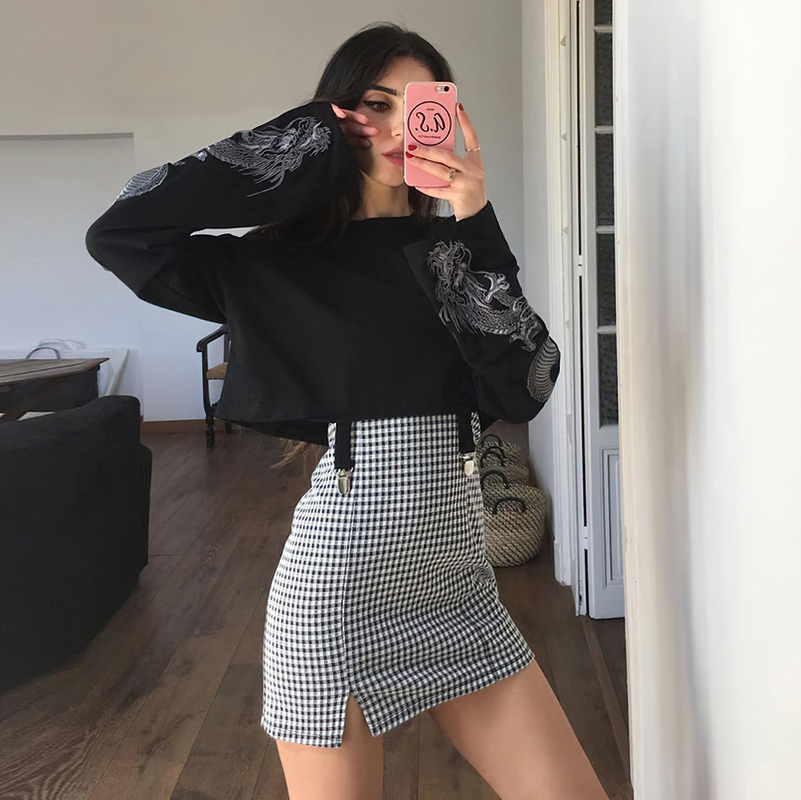 Fashionable women's black loose pullover with dragon print, styled with a checkered skirt, perfect for casual outings.
