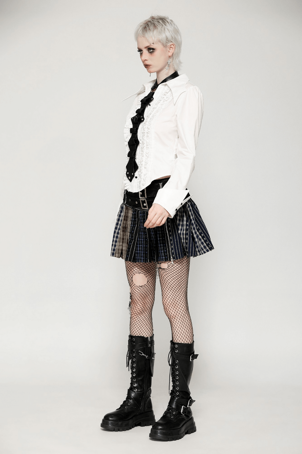 Alternativer fashion model in a ruffled white shirt, plaid skirt, fishnet tights, and combat boots, showcasing edgy style.