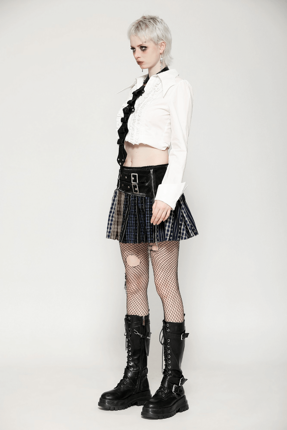 Model showcasing edgy punk fashion with a cropped shirt, plaid skirt, fishnet tights, and combat boots.
