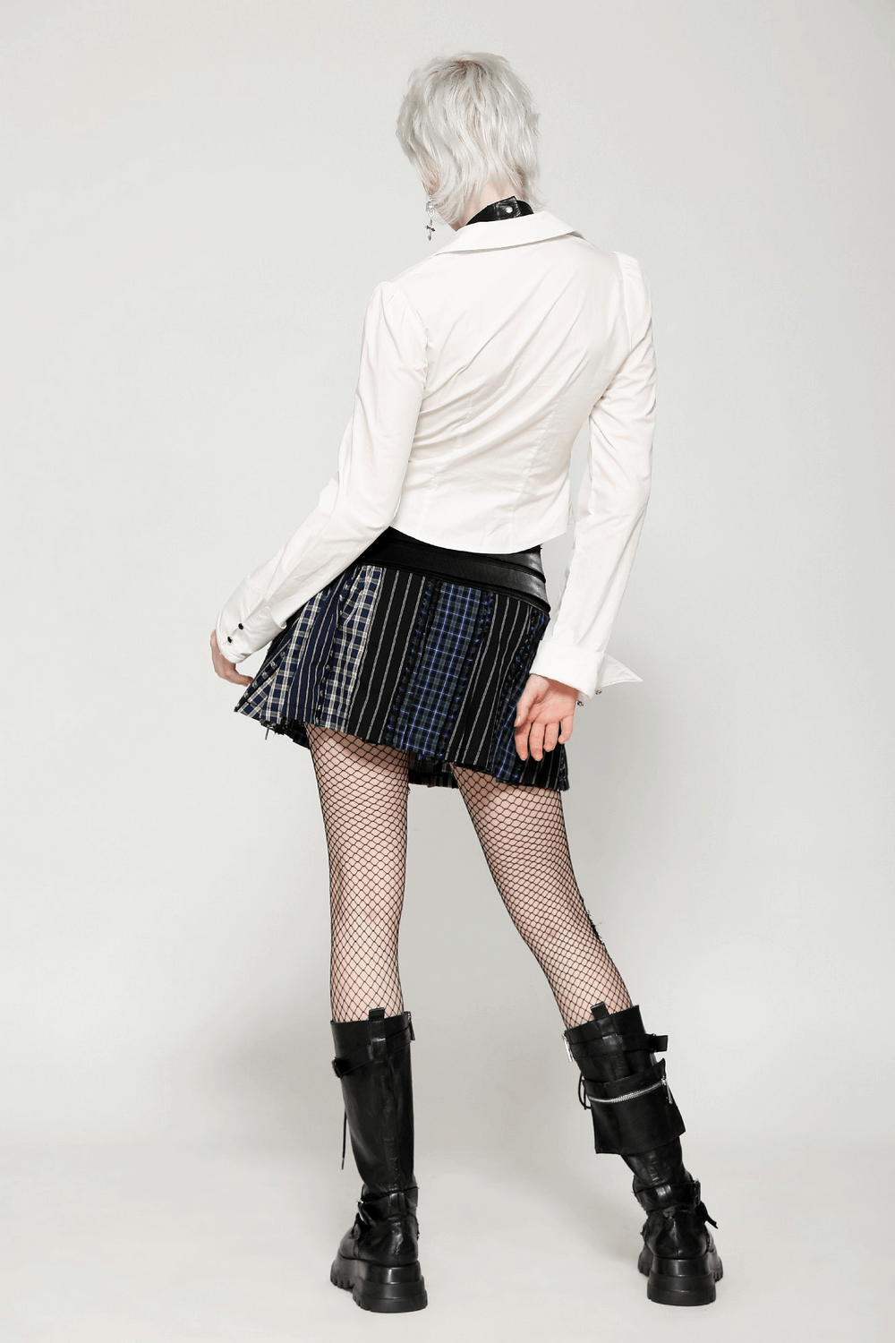 Alternative fashion model wearing a faux leather skirt and white top with fishnet stockings and black boots.