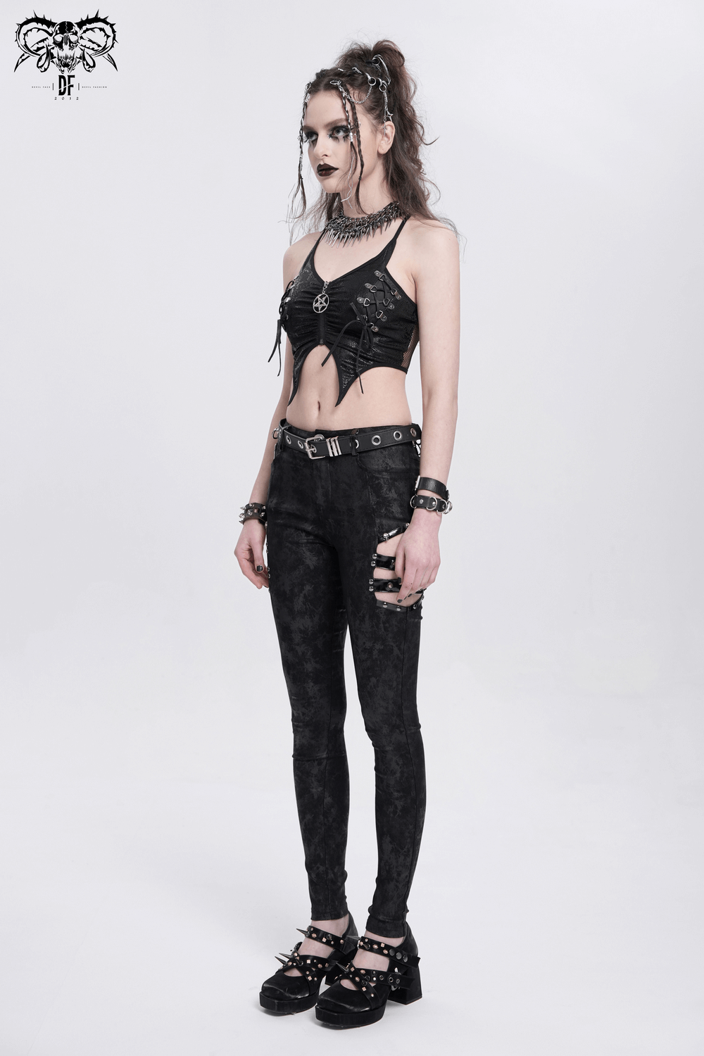 Edgy female model in black sleeveless crop top with pentagram and strappy design, paired with black skinny pants.