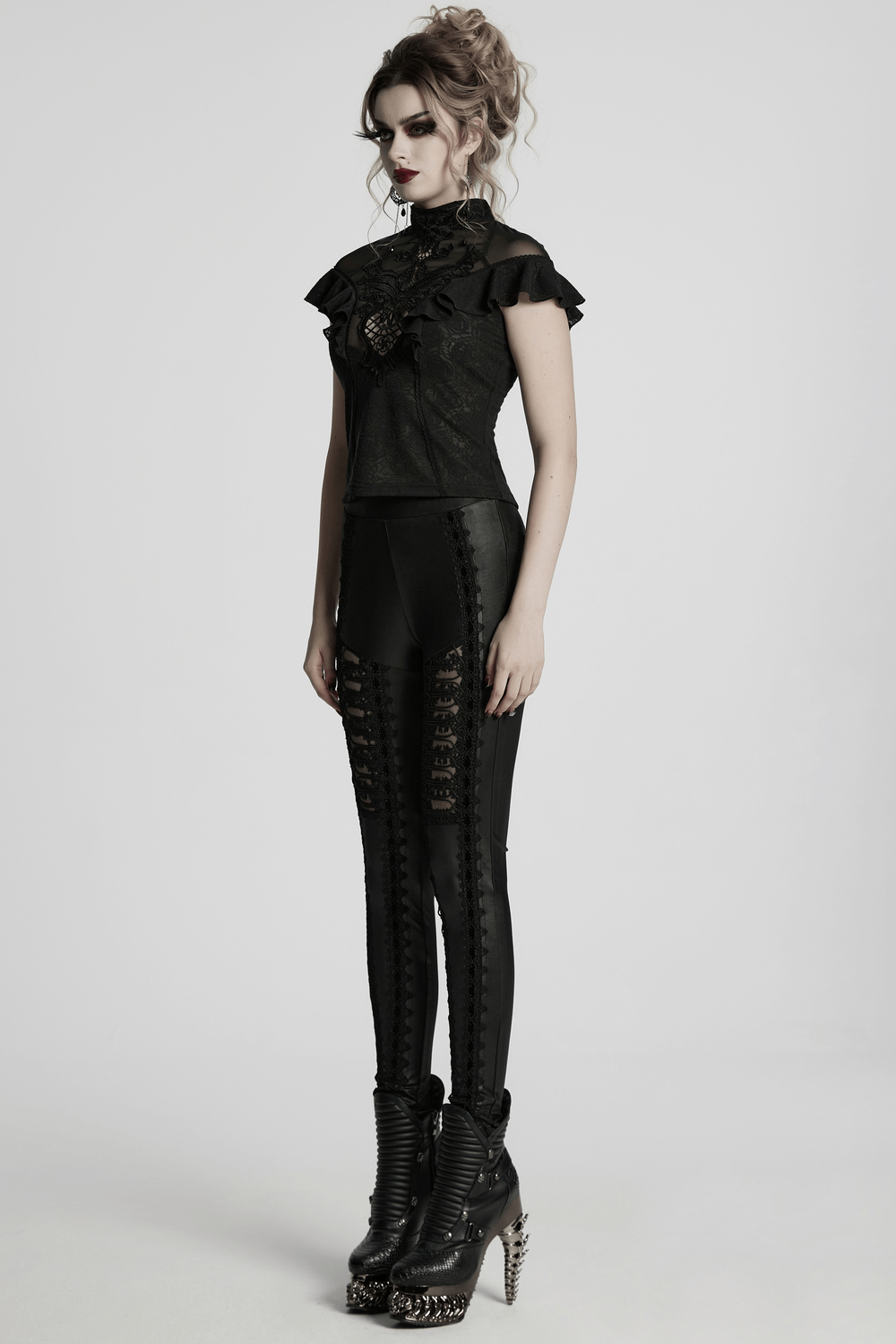 Female model wearing glossy black lace spliced gothic leggings, styled with a ruffled top and edgy ankle boots.