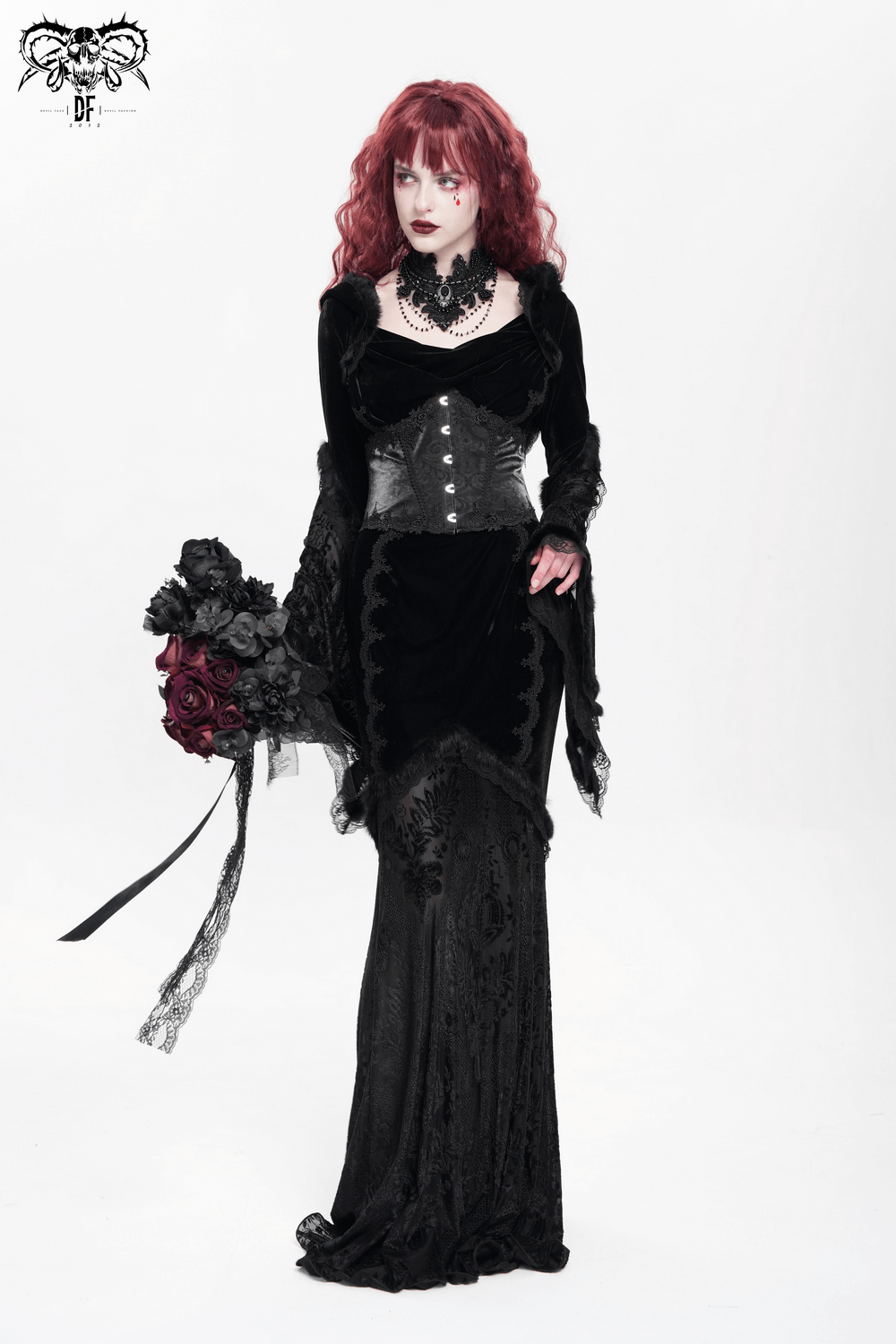 Gothic female model in a long black velvet hooded dress with lace and corset details, holding a bouquet of dark roses.