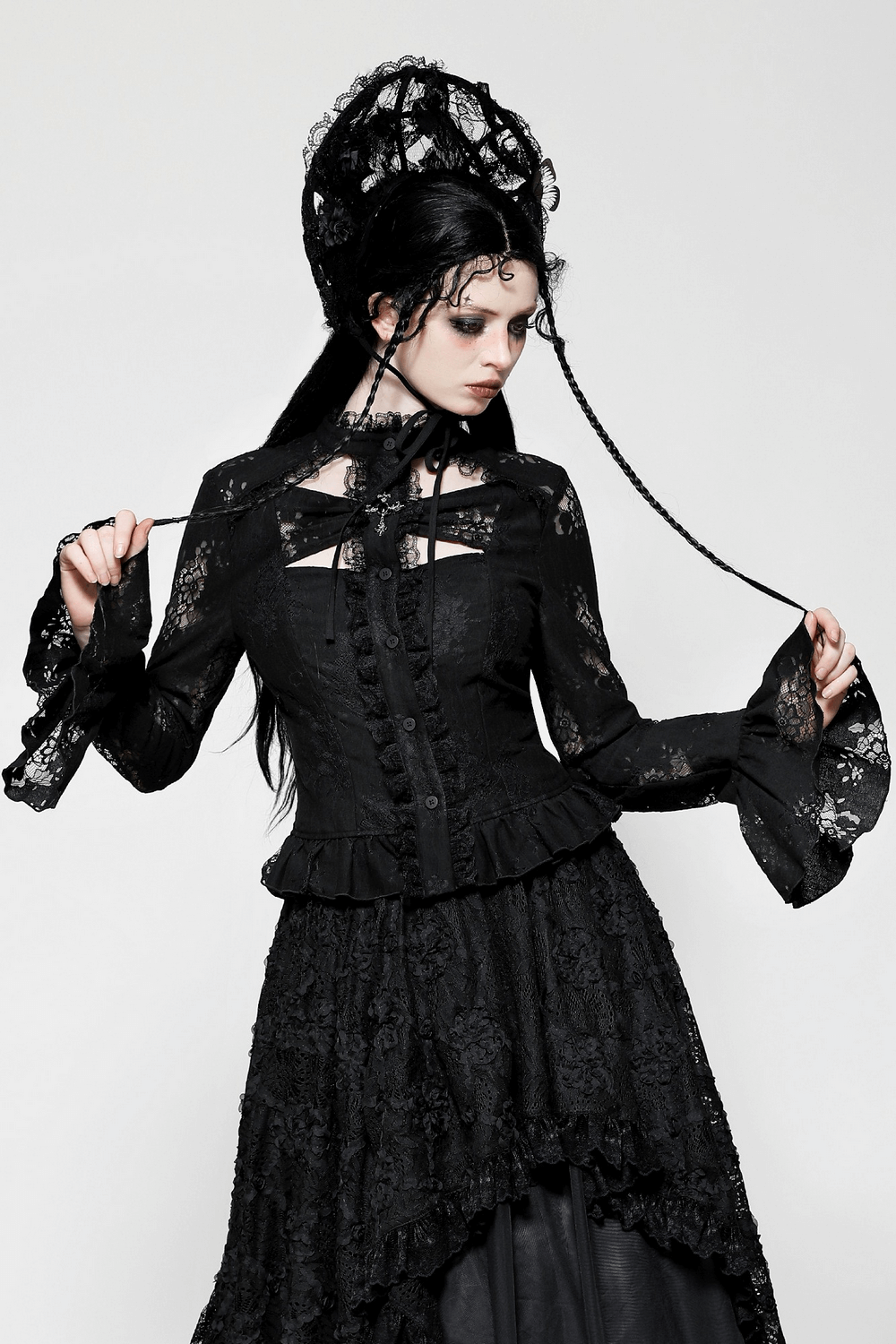 Stylish female model in black gothic lace blouse with cross, cutouts, and bell sleeves, showcasing a darkly elegant look.