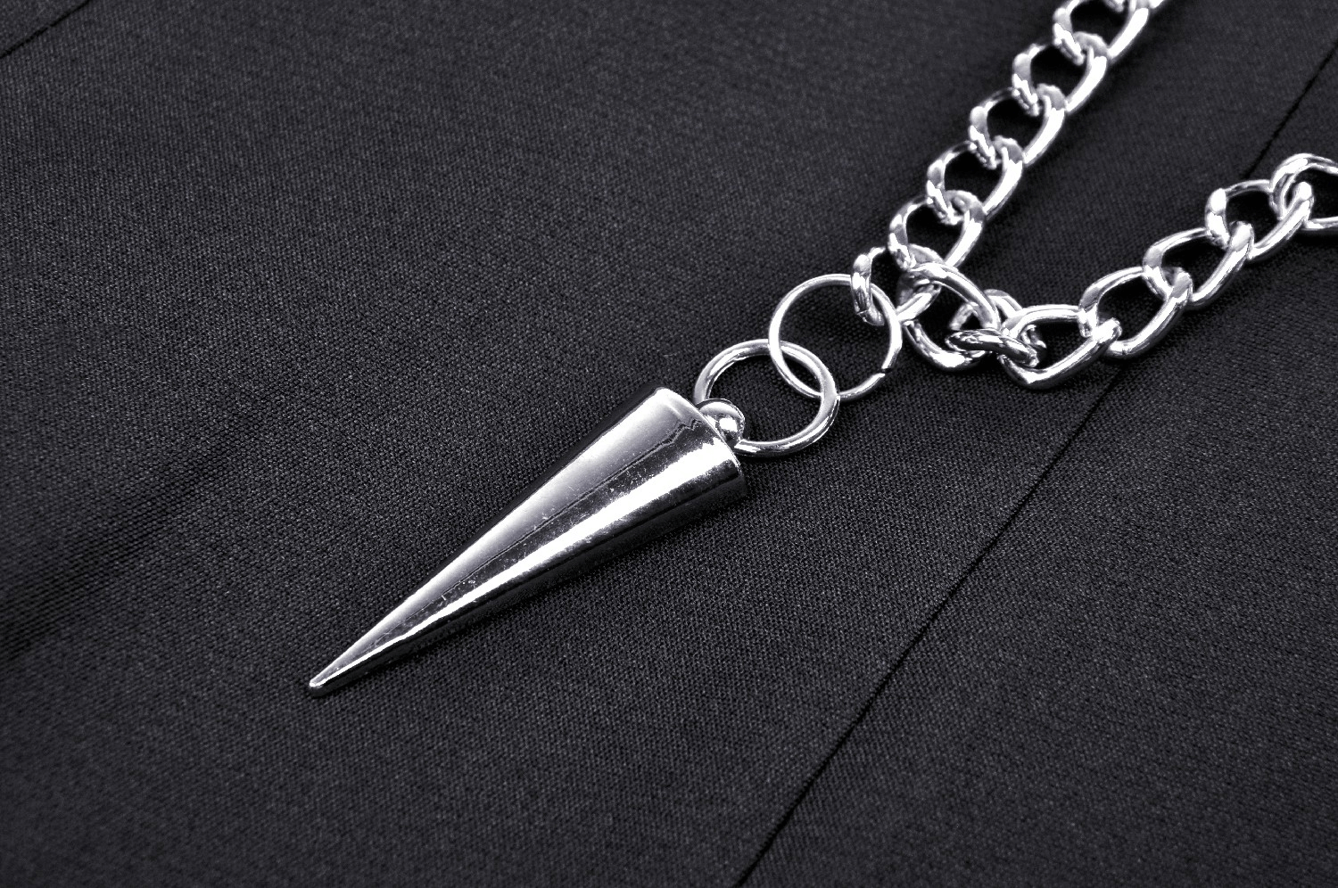 Close-up of silver chain with spike pendant on a black pleated mini skirt, adding edgy gothic flair.