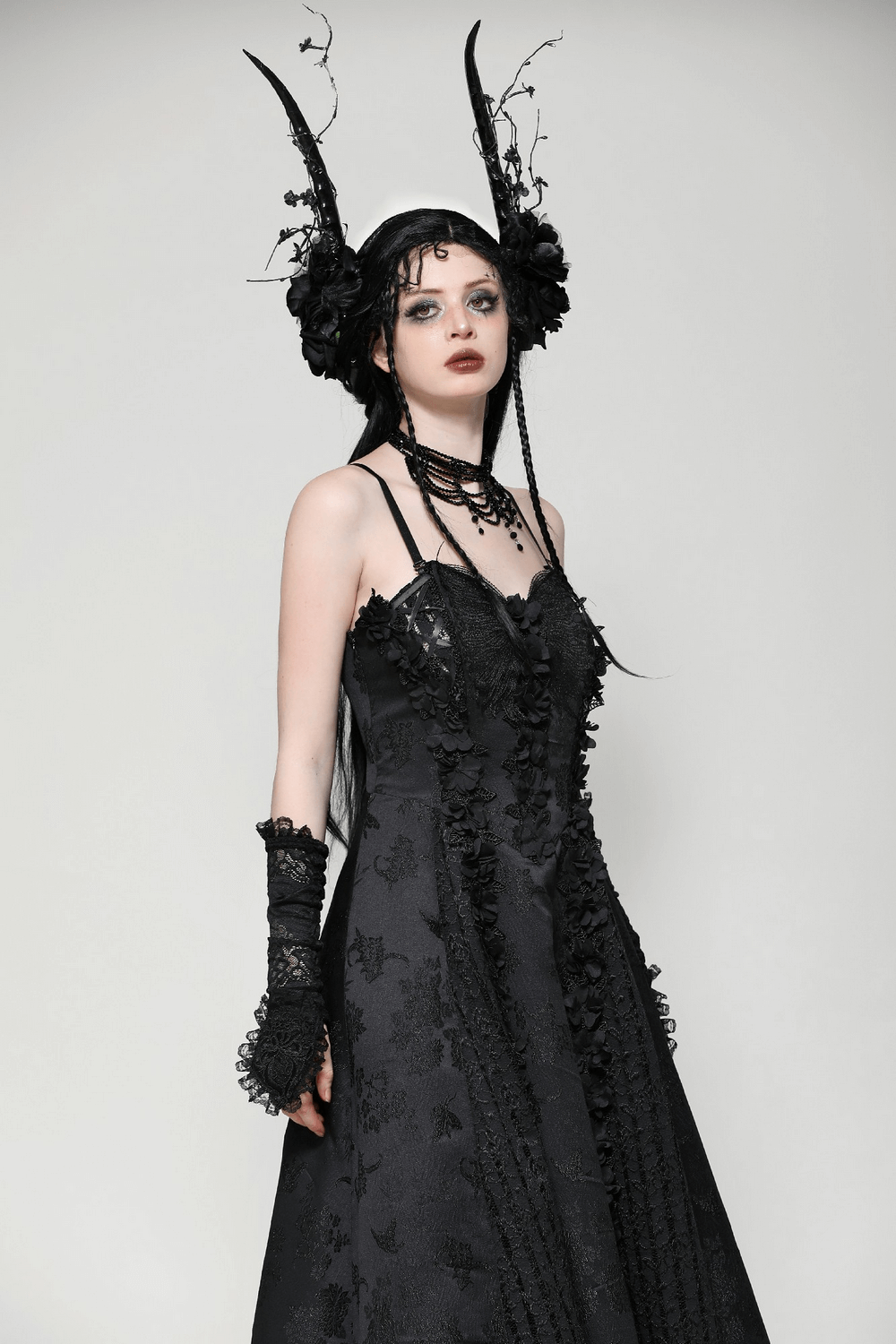 Female model in gothic black lace maxi dress with floral details and striking accessories, showcasing dark elegance.