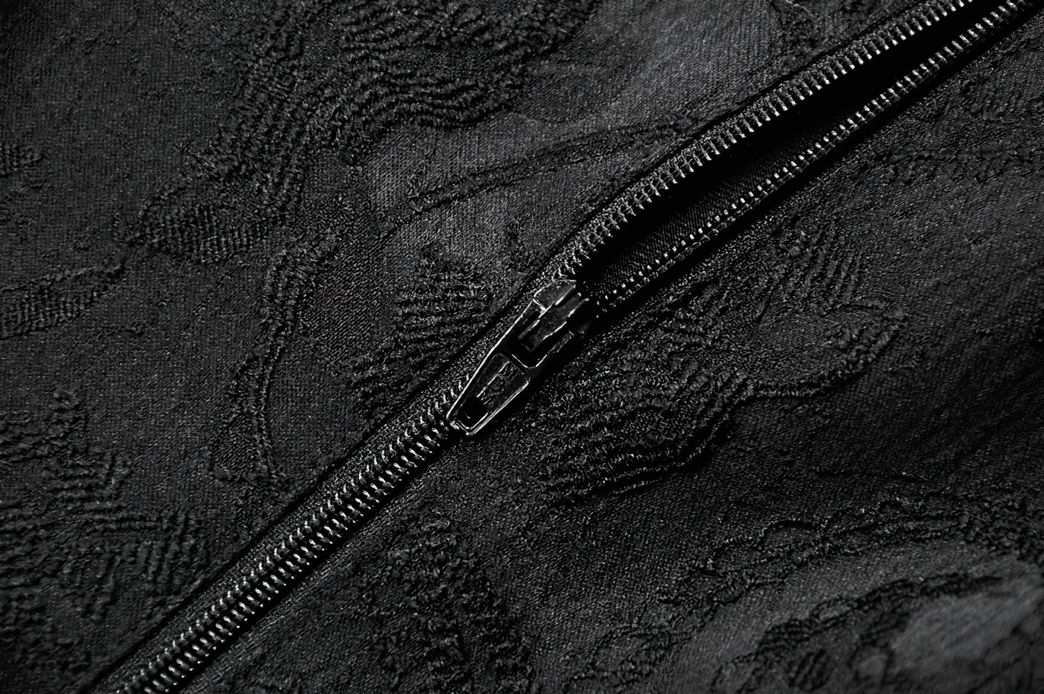 Close-up of a black lace fabric showing intricate embroidery and a zipper detail for elegance.