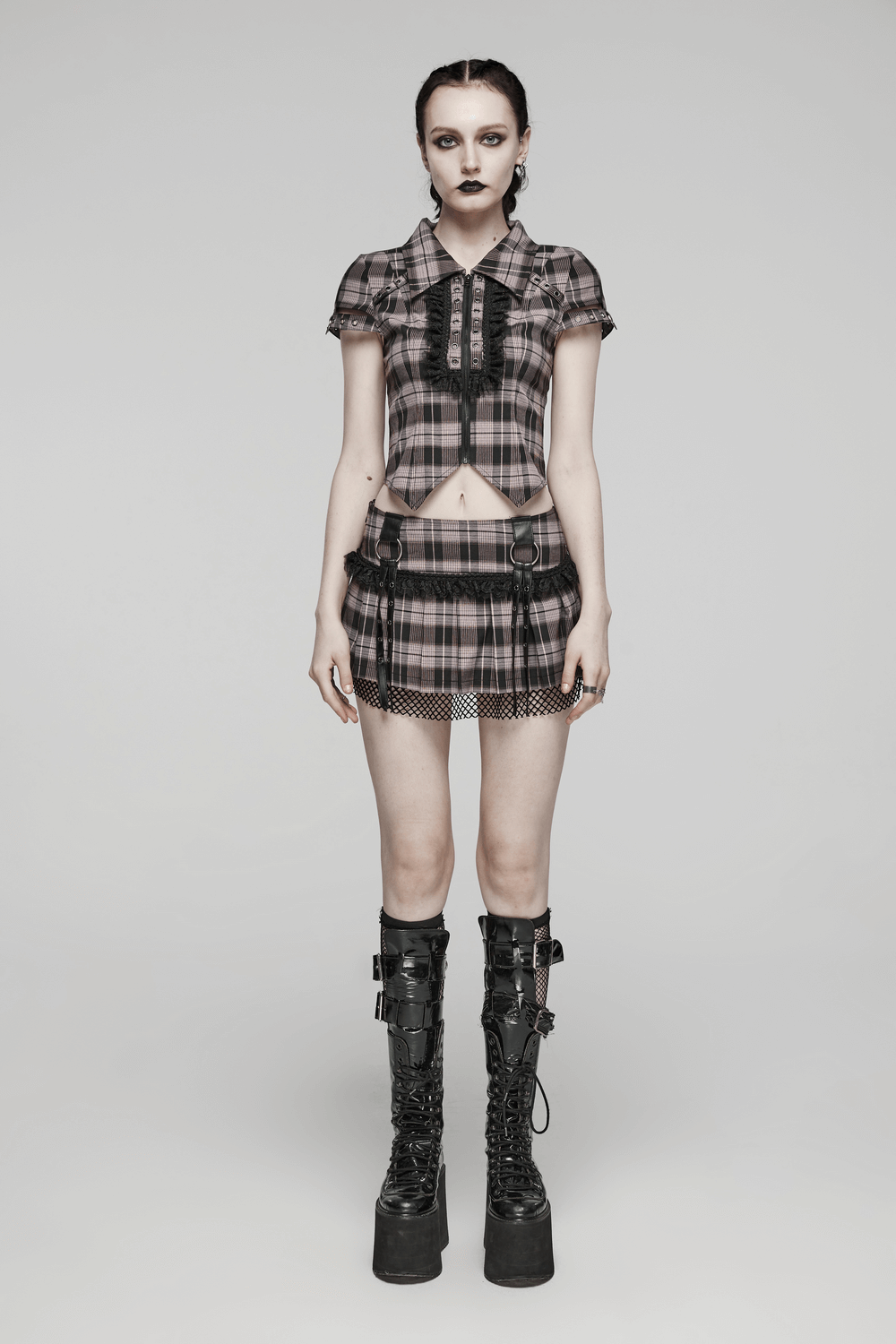 Model wearing a black and pink plaid mini skirt with fishnet overlay and edgy combat boots.