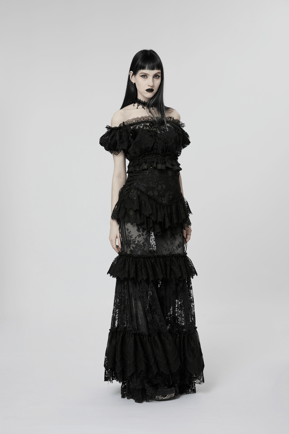 Elegant gothic model in layered black lace dress with off-shoulder design and dark lipstick.