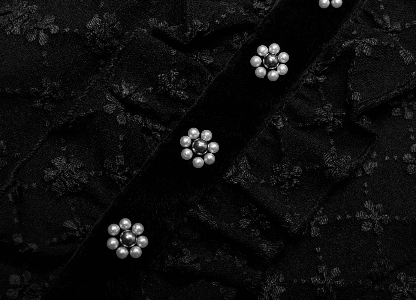 Close-up of black floral jacquard fabric with pearl-accented velvet ribbon on a whimsical dress.