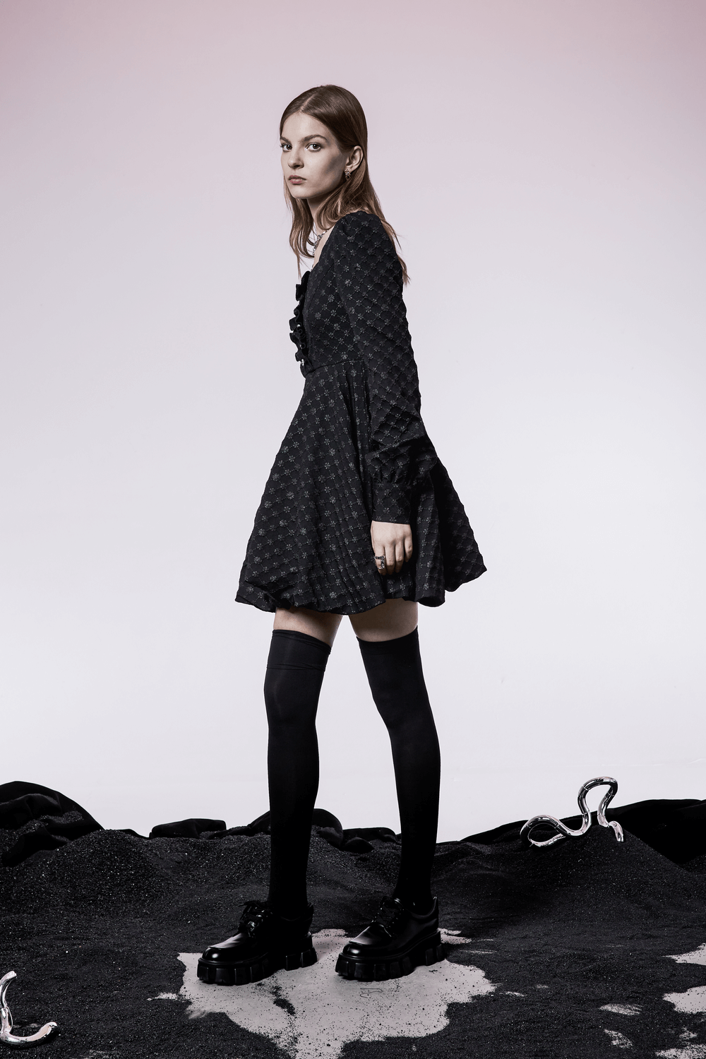 Model wearing a stylish black floral dress with long sleeves and knee-high socks, against a minimalist background.