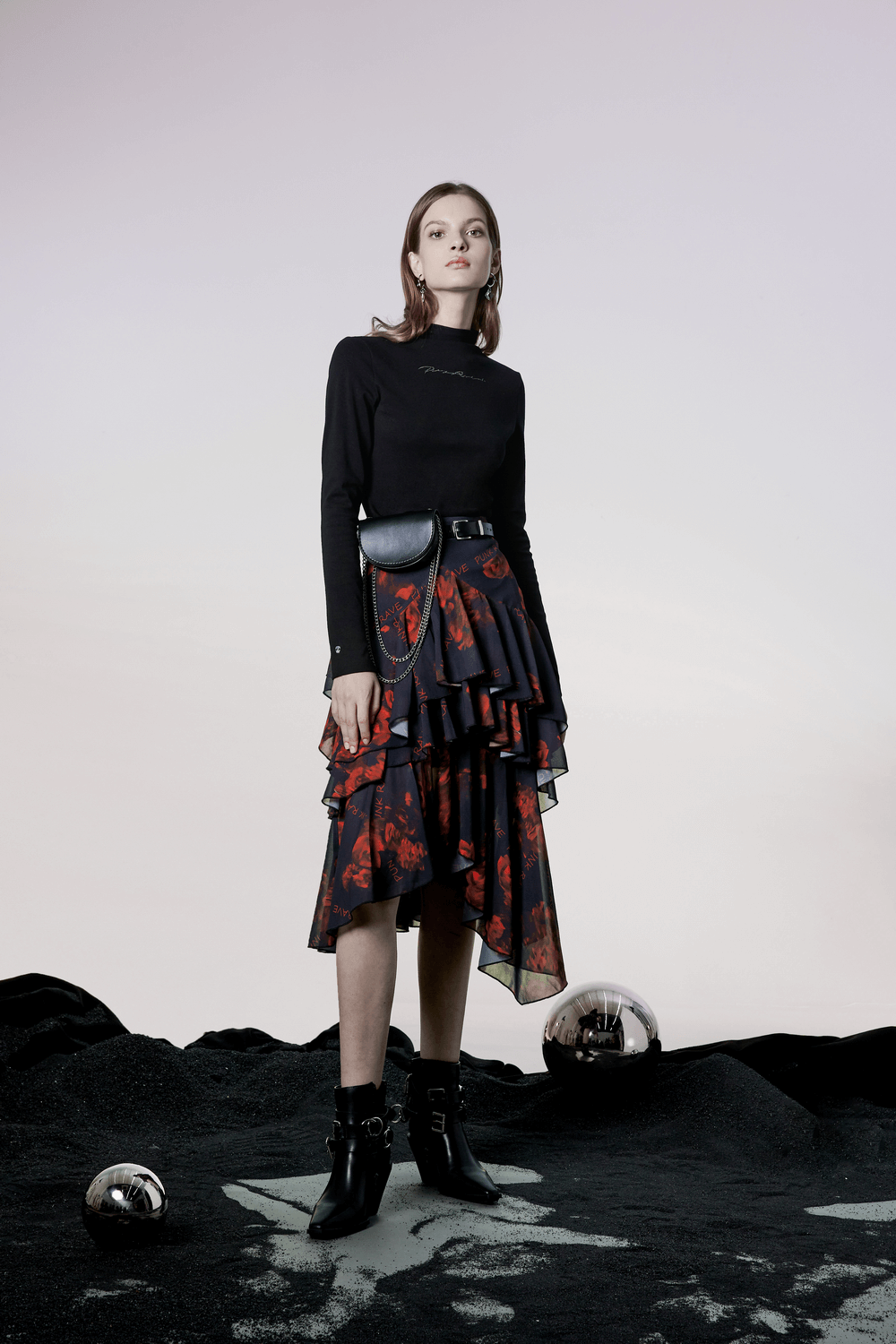 Model showcasing a high-low floral layered skirt with edgy black top and accessories against a minimalist background.