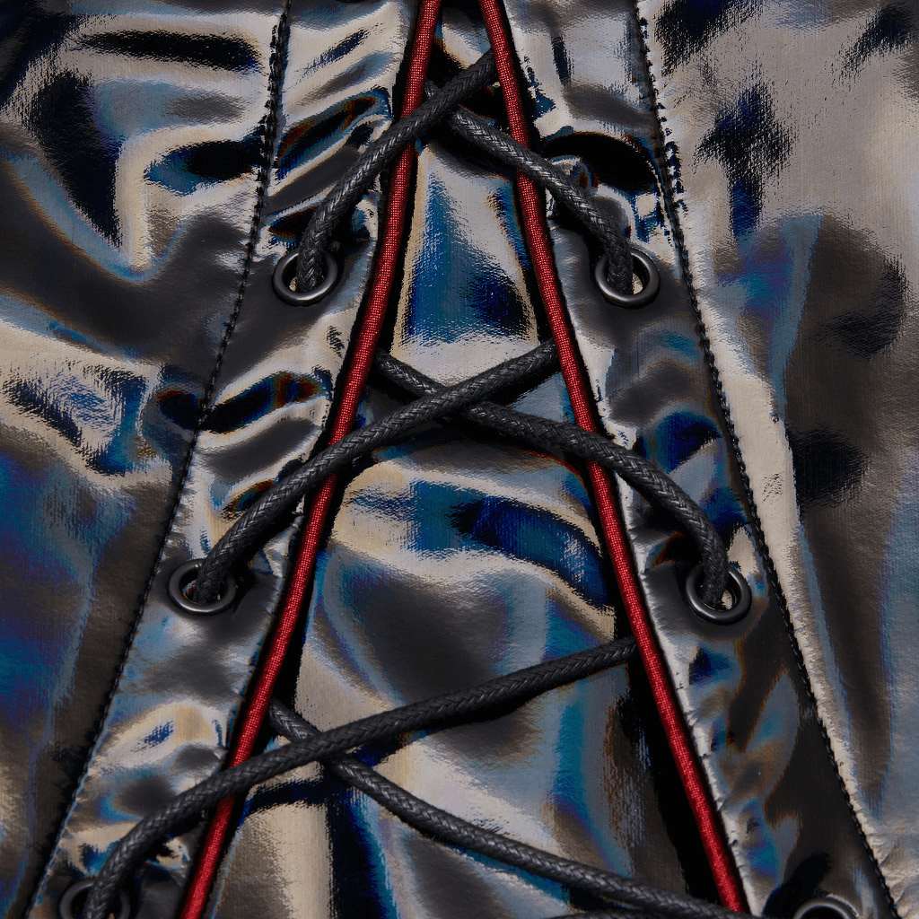 Close-up of futuristic laser-cut fabric with red accents and intricate lacing detail in avant-garde style coat.