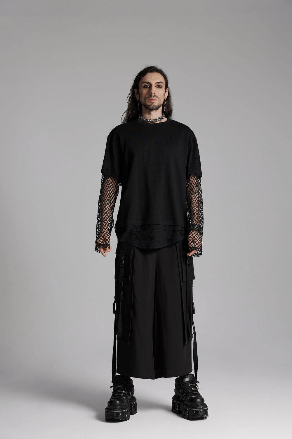 Model in black oversized shirt with fishnet sleeves and wide pants, showcasing edgy alternative fashion style.