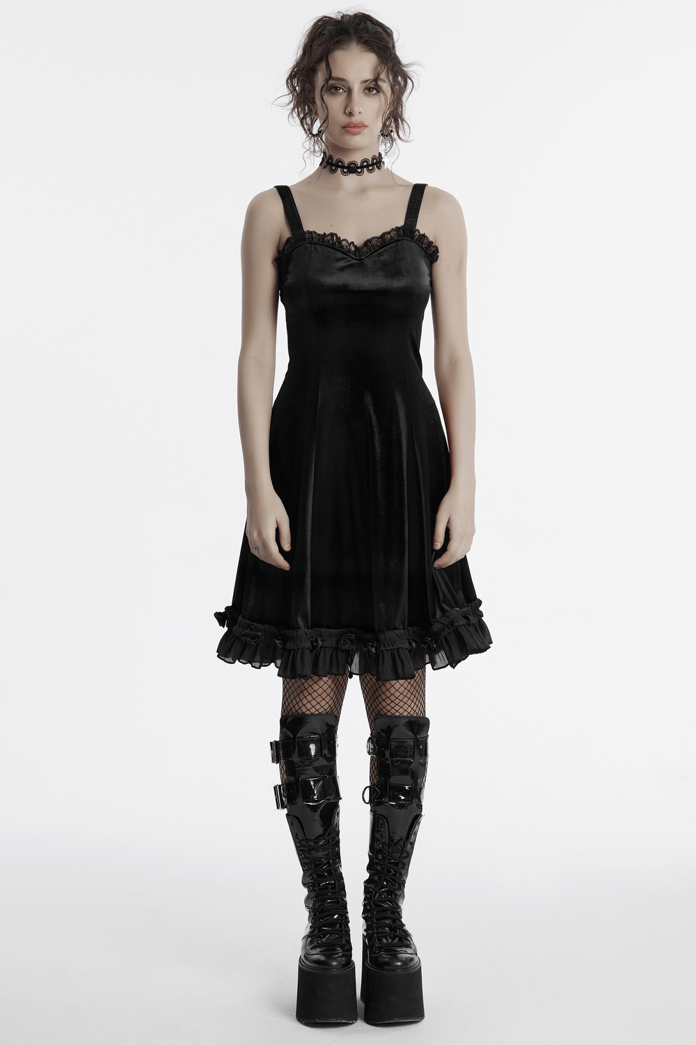 Elegant goth black velvet dress with lace details and ruffled hem, styled with bold boots and a choker.