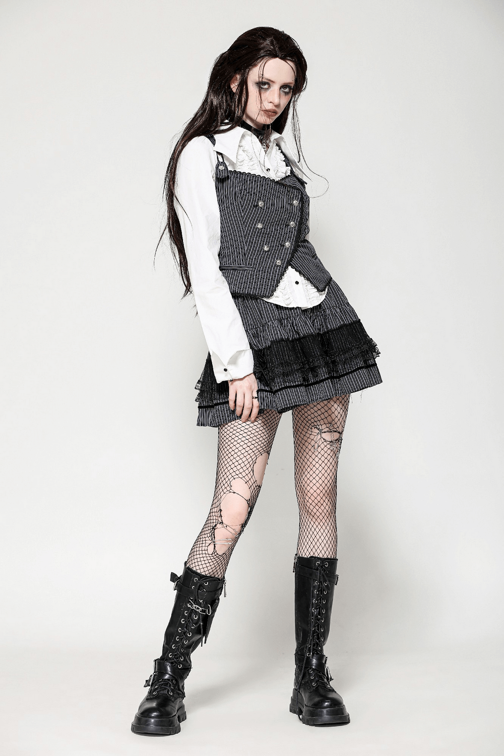 Goth model wearing a pinstripe double-breasted vest with straps, paired with a frilly skirt and fishnet tights.