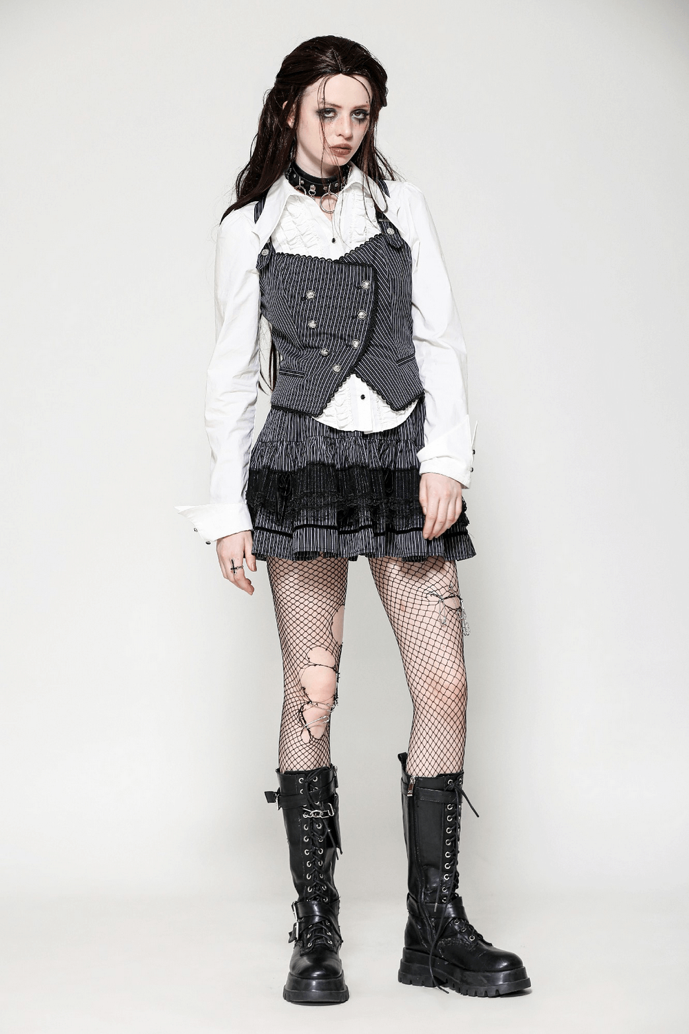 Gothic model wearing a pinstripe double-breasted vest with straps, paired with a frilly skirt and combat boots.