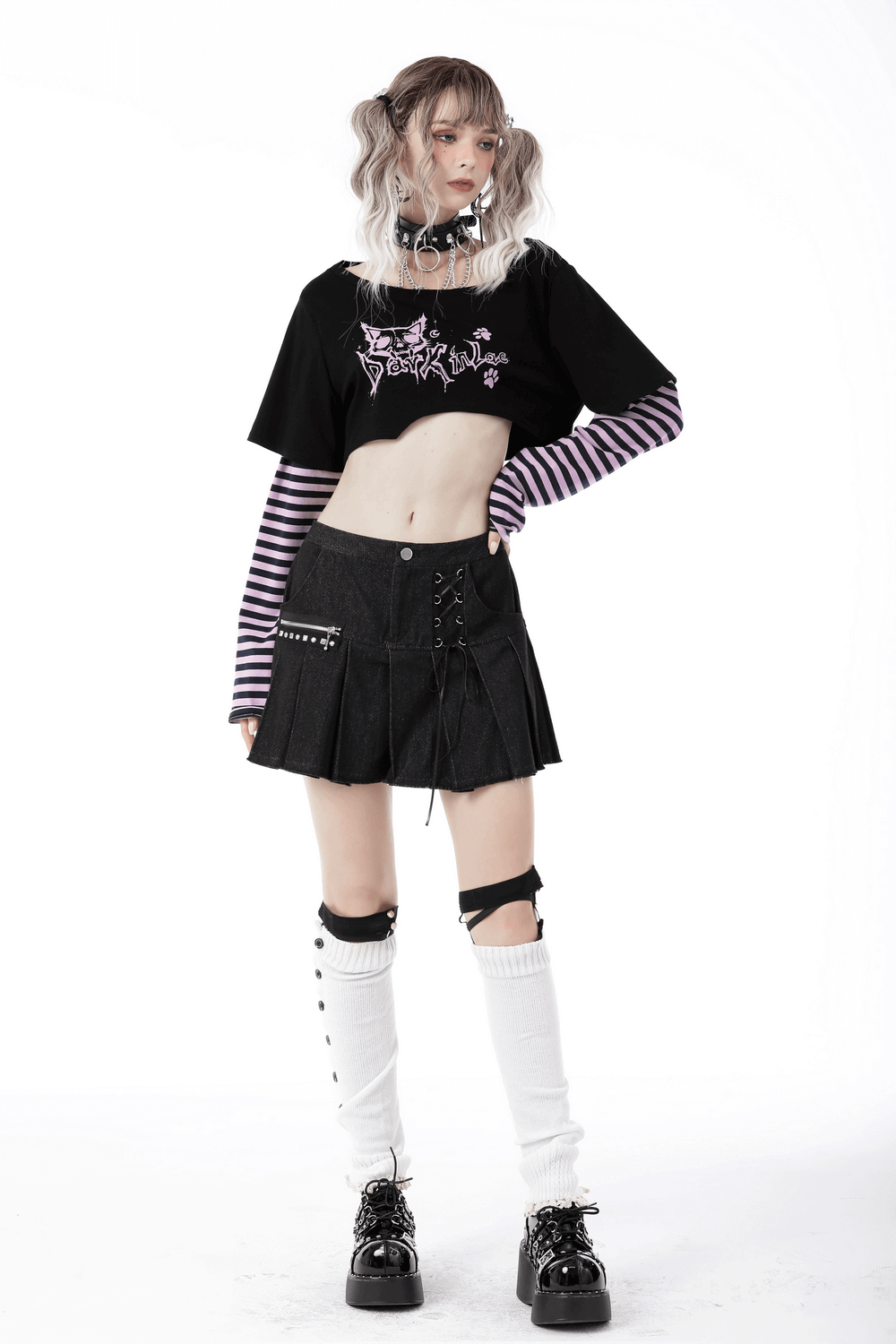 Goth punk crop top with Cheshire Cat graphic, striped sleeves, paired with a black pleated skirt and stylish accessories.