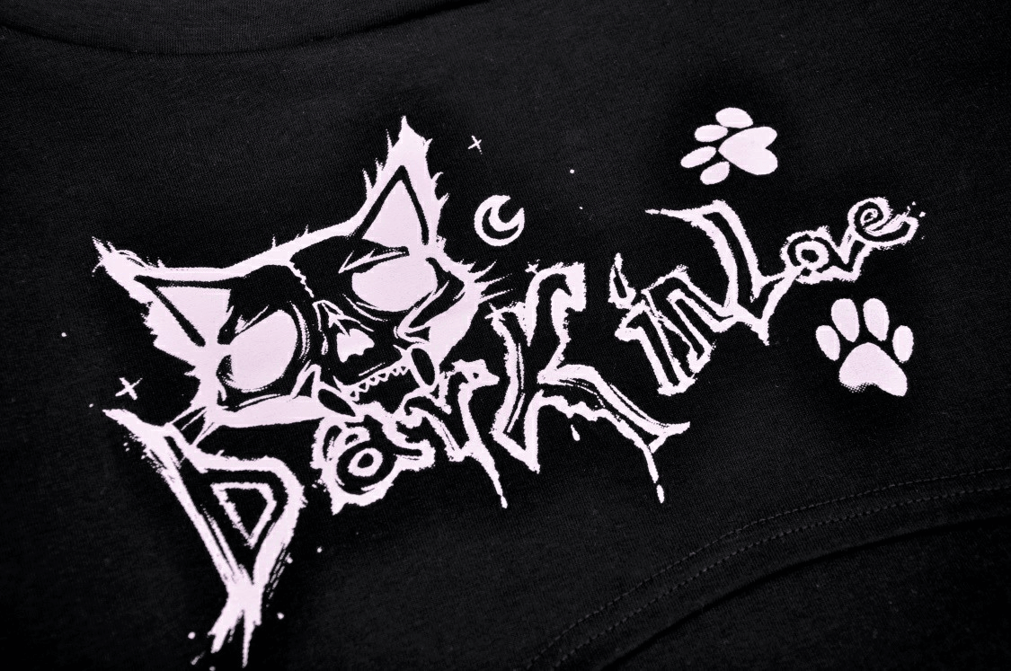 Gothic graphic design of a skull Cheshire Cat with text 'Dark in Love' and paw prints on black fabric.