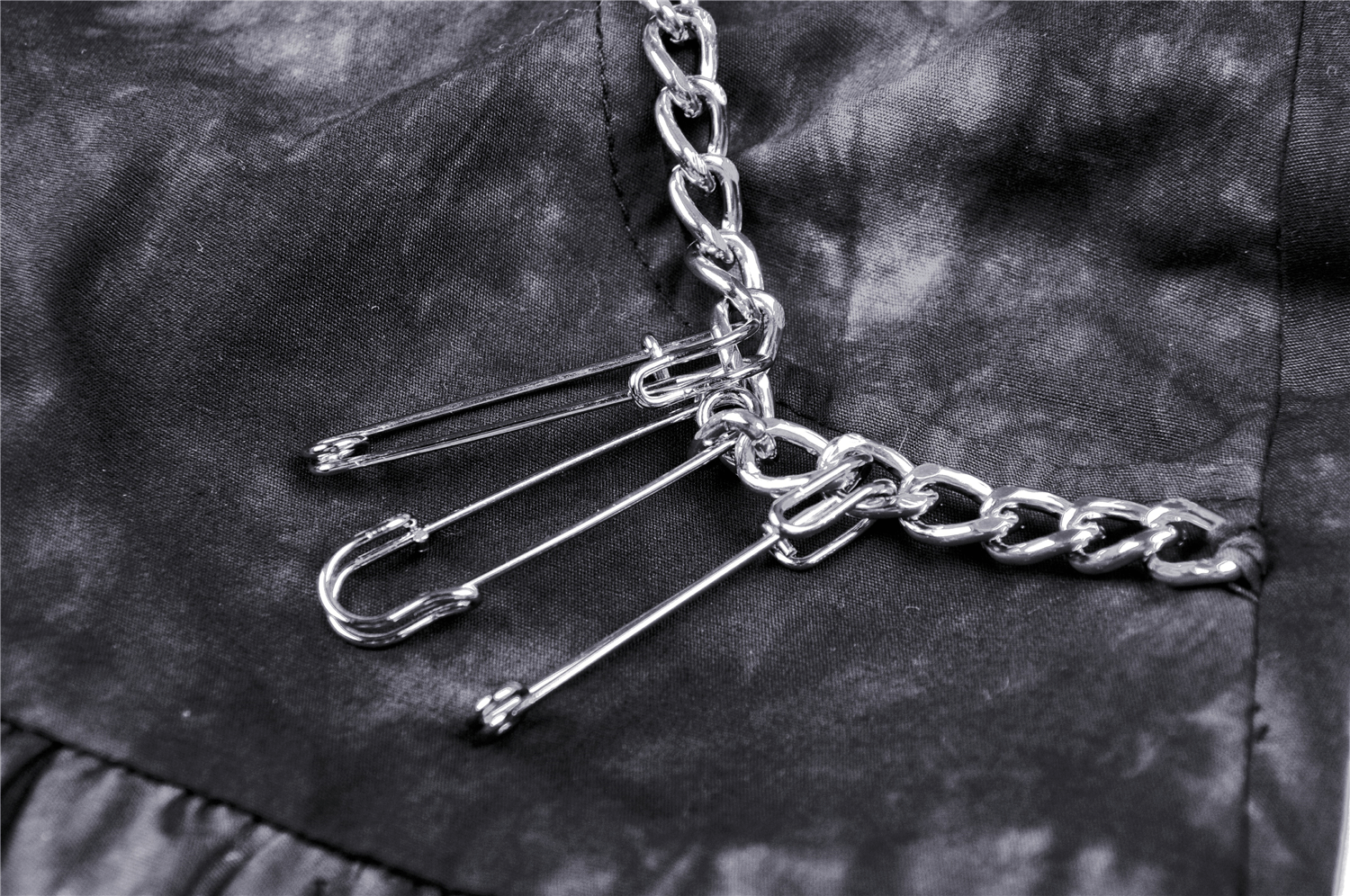 Close-up of silver chains and safety pins on a goth mini skirt, showcasing edgy details.