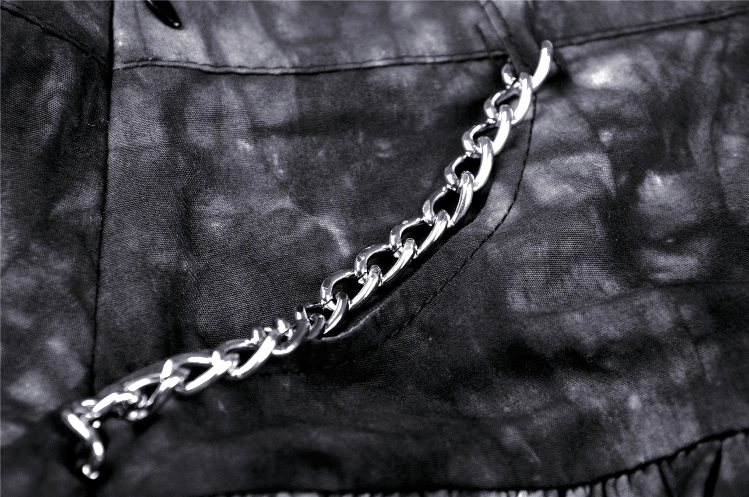 Close-up of a black mini skirt featuring a stylish silver chain detail and ruffled texture, perfect for goth fashion.