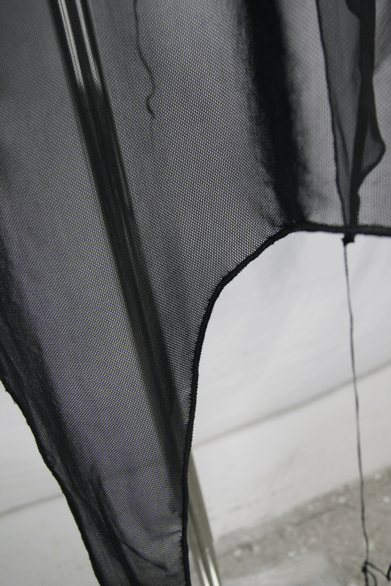 Close-up of a sheer black mesh fabric showcasing the asymmetrical cut of a gothic hooded cape.