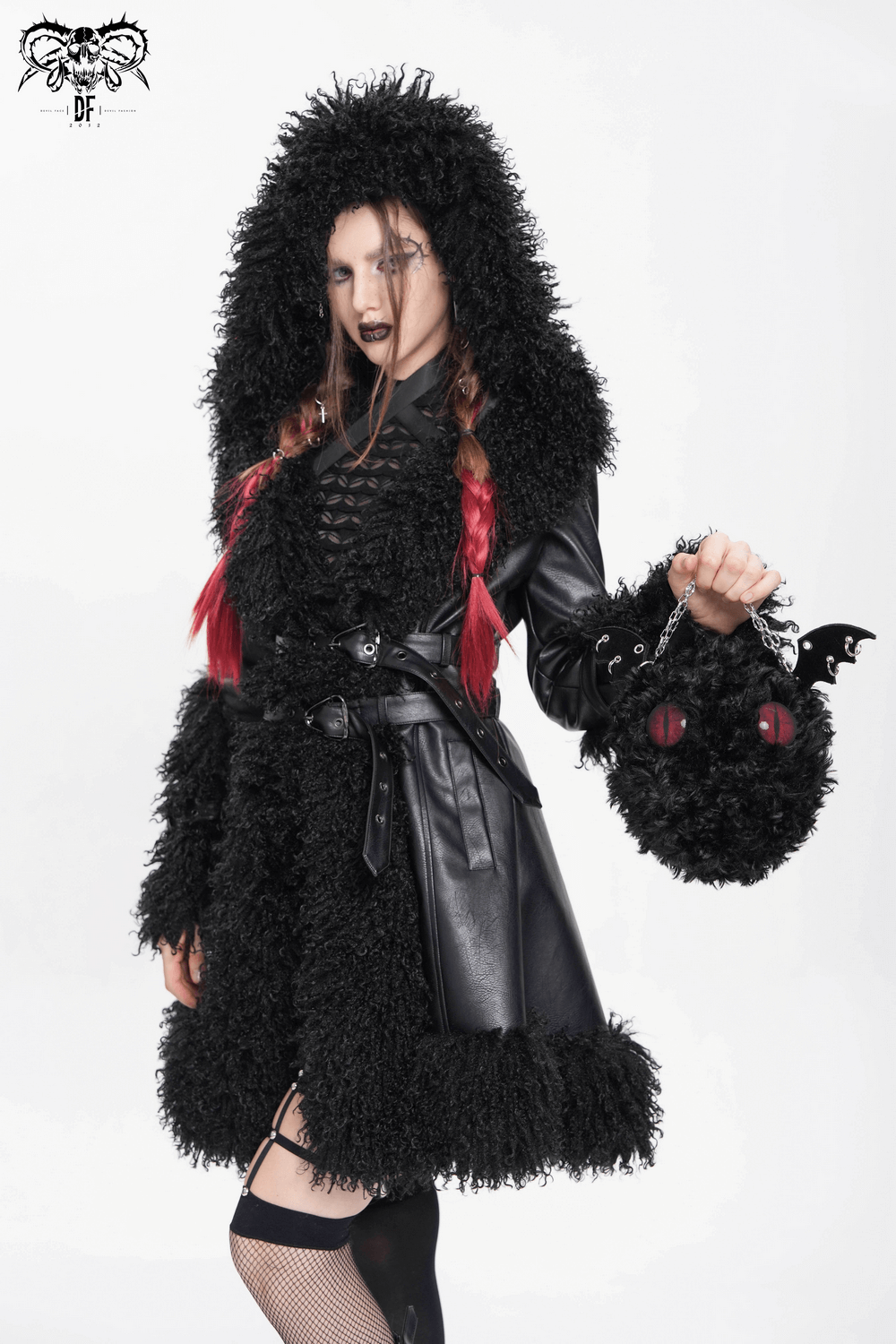 Gothic model in fluffy black coat with hood, holding plush bat wing bag with red eyes, showcasing alternative fashion.