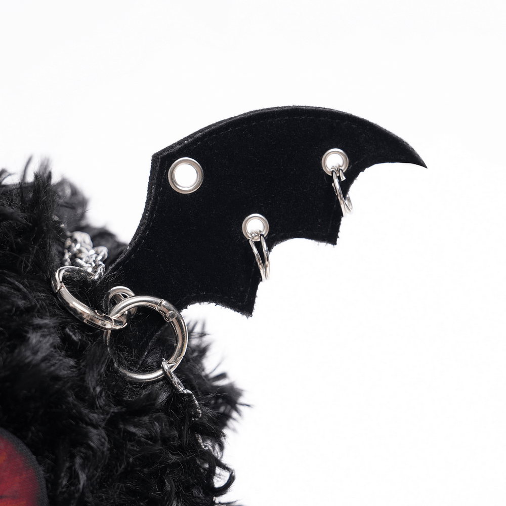 Close-up of bat wing detail on a plush goth shoulder bag, showcasing silver chain charm and faux fur texture.