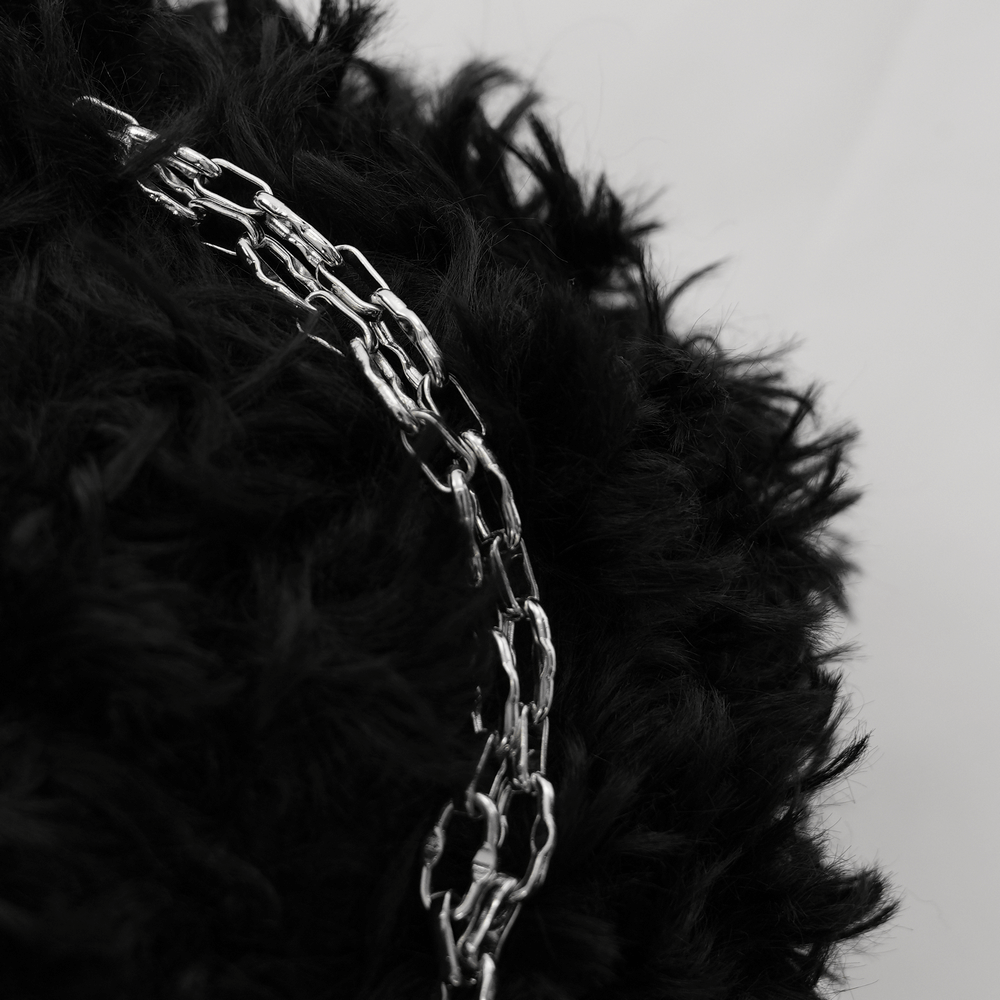 Close-up of silver chain resting on plush black faux fur, ideal for gothic or alternative fashion accessories.