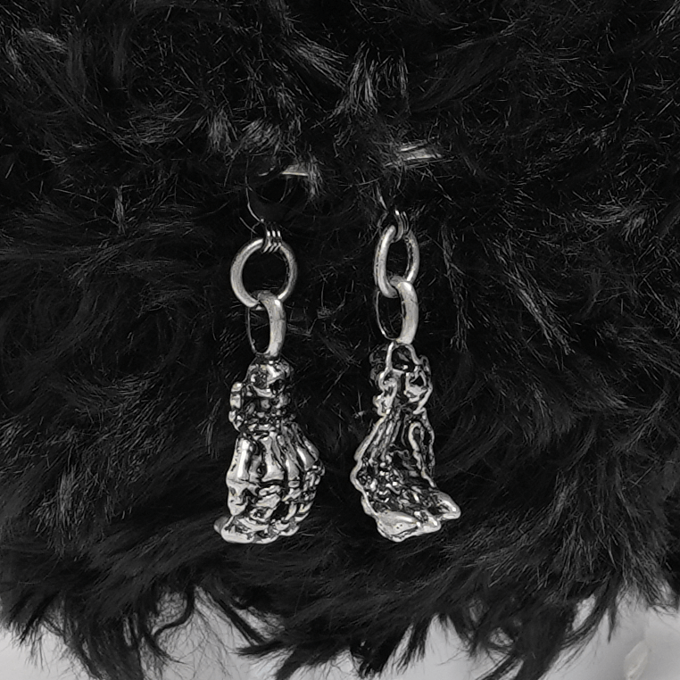Close-up of silver skeleton hand charms on a plush black bag, adding gothic flair to alternative fashion.