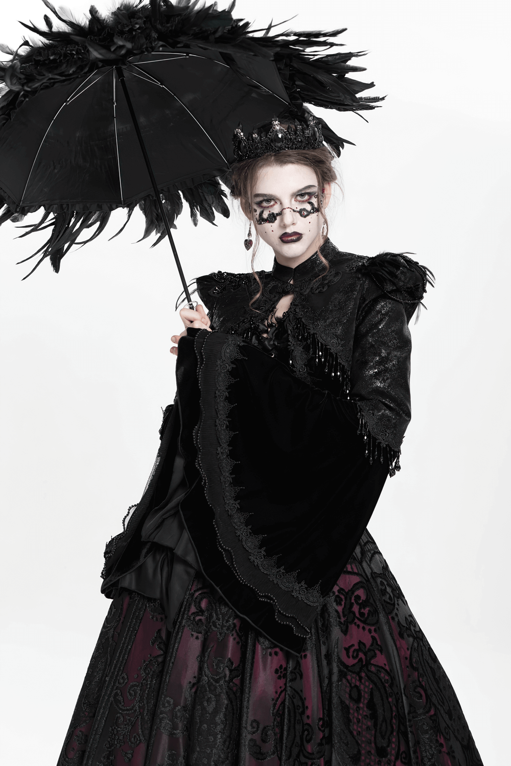 Gothic woman in black bolero shrug with lace and beaded sleeves, holding a feathered umbrella, showcasing dark elegance.