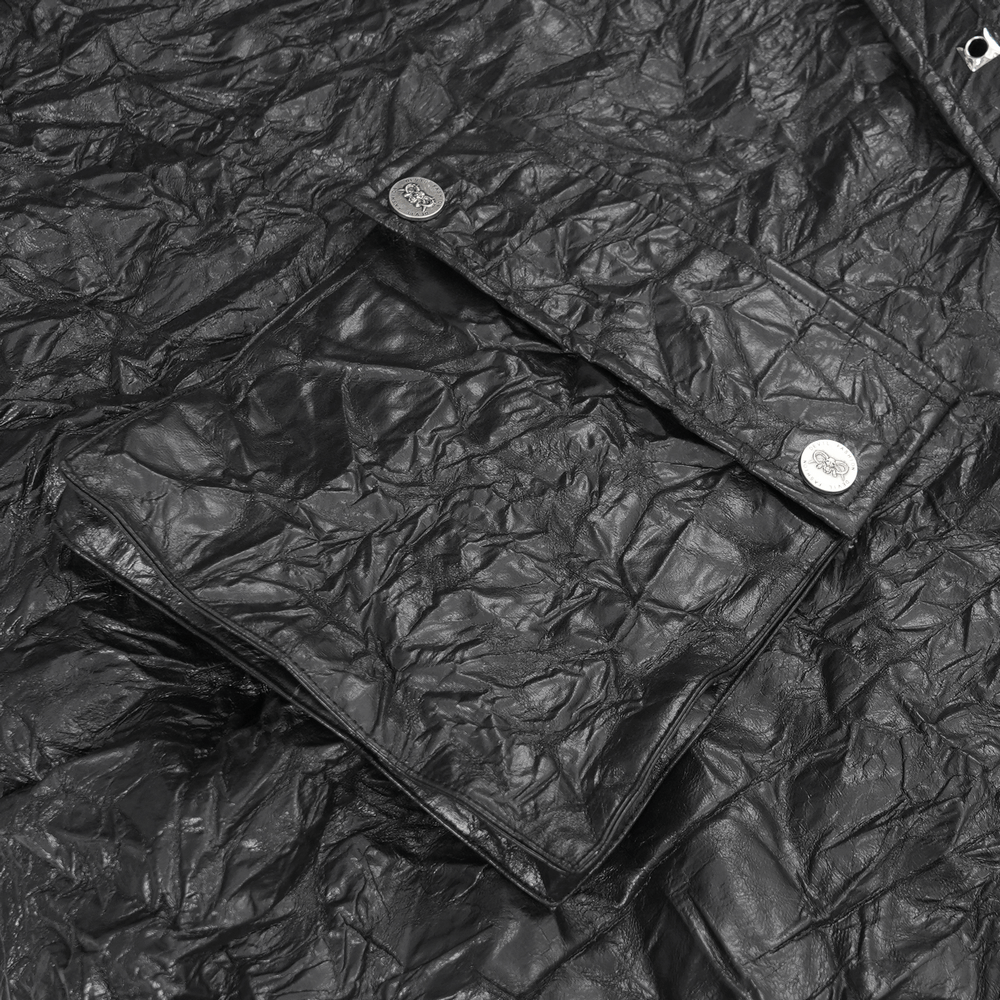 Close-up of crinkled black leather showcasing a pocket and metallic button on a Gothic-inspired kilt.