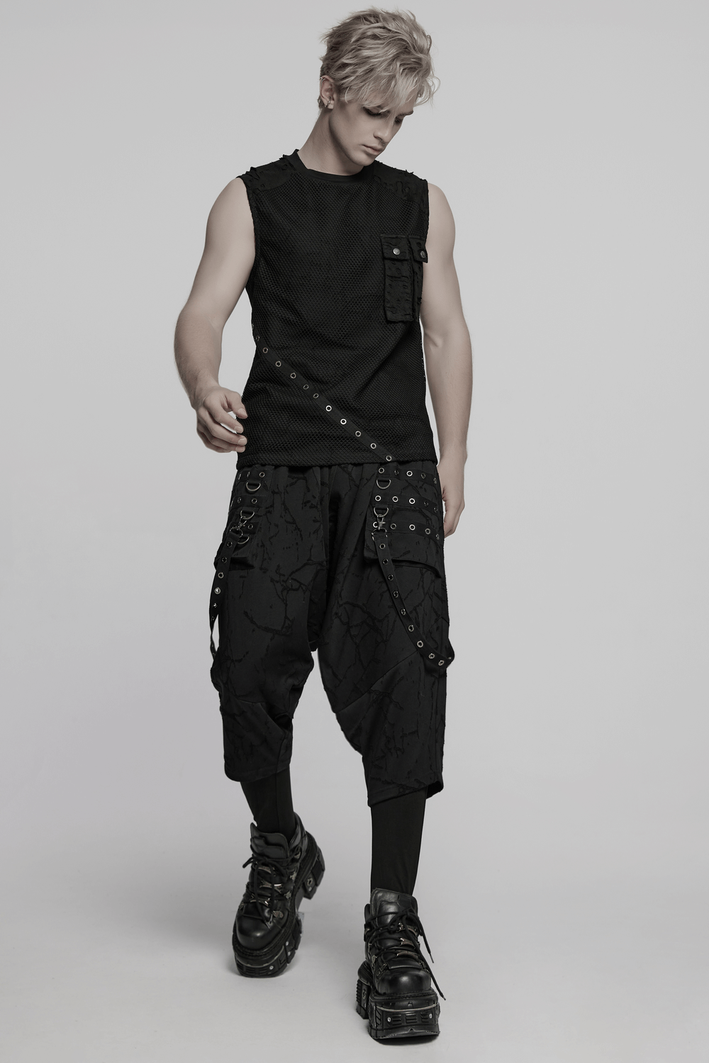 Male model in gothic black drop crotch pants with eyelet straps and sleeveless top, showcasing punk style.