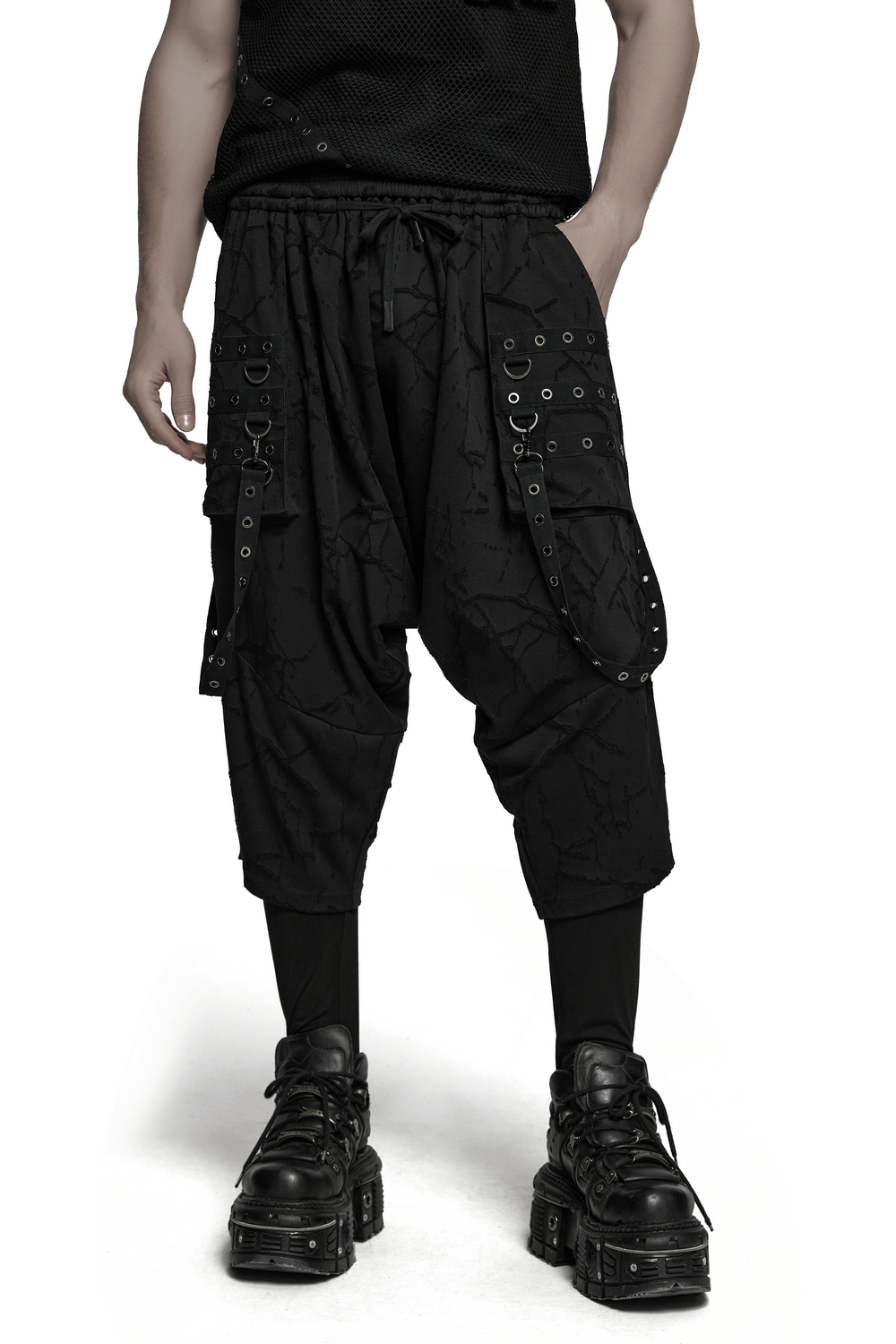 Gothic black drop crotch pants with eyelet straps, featuring a relaxed fit and bold pockets, styled with edgy footwear.