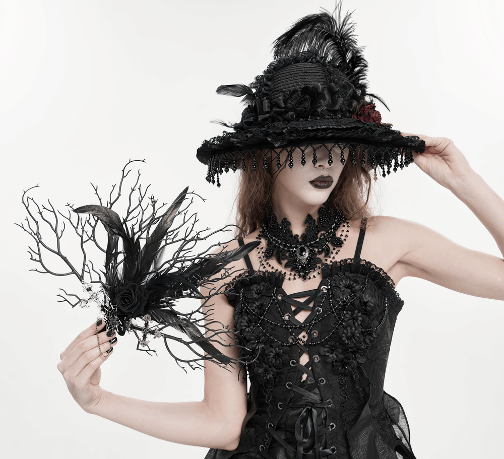 Gothic Black Feather and Twig Hand Fan with Cross Charms held by a model in a gothic outfit and hat.