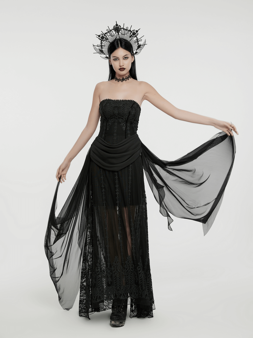 Elegant model in a gothic black floral mesh dress with chiffon layers and a striking crown, showcasing intricate embroidery.