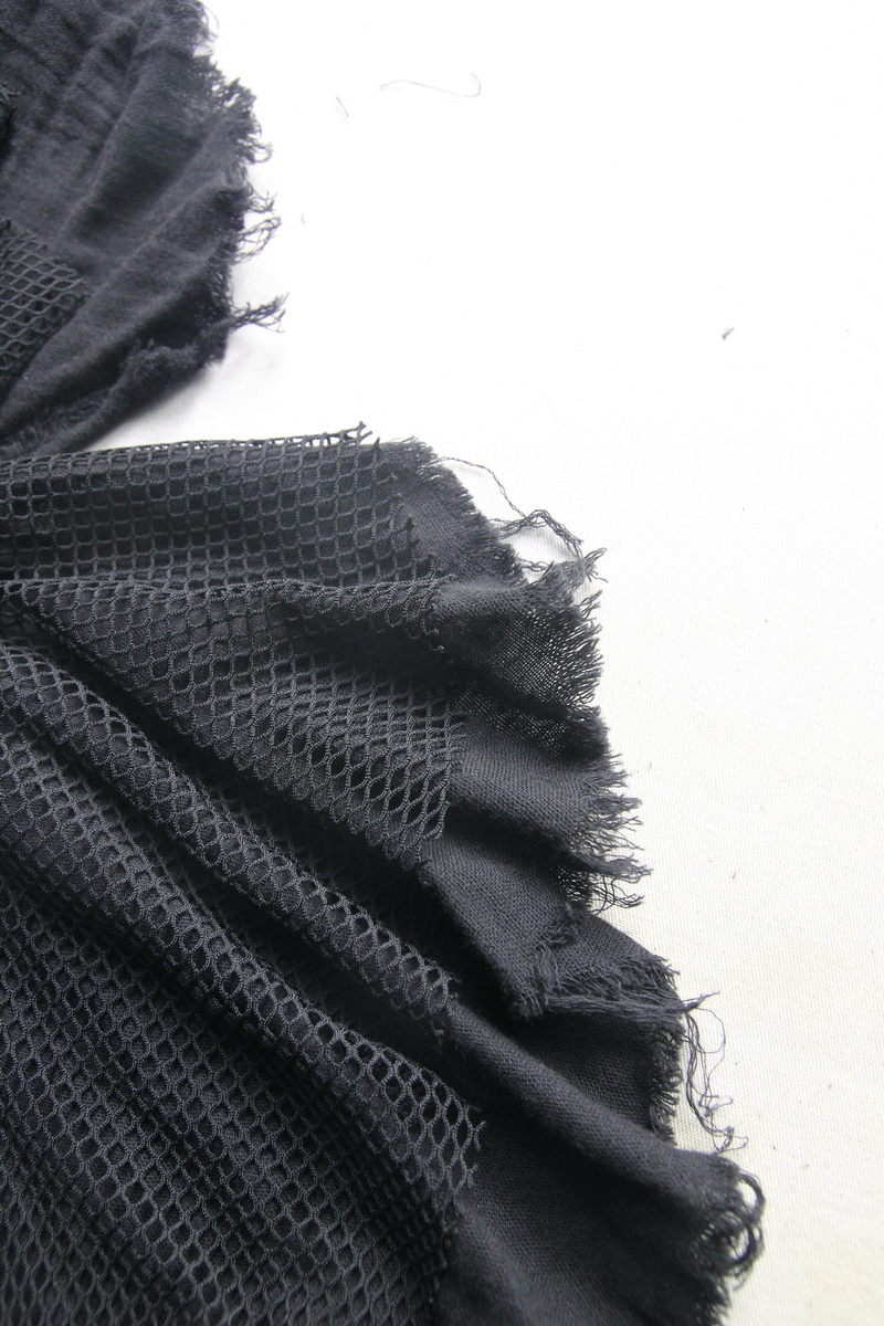 Close-up of black irregular skirt fabric showcasing textured mesh and frayed edges for gothic fashion.