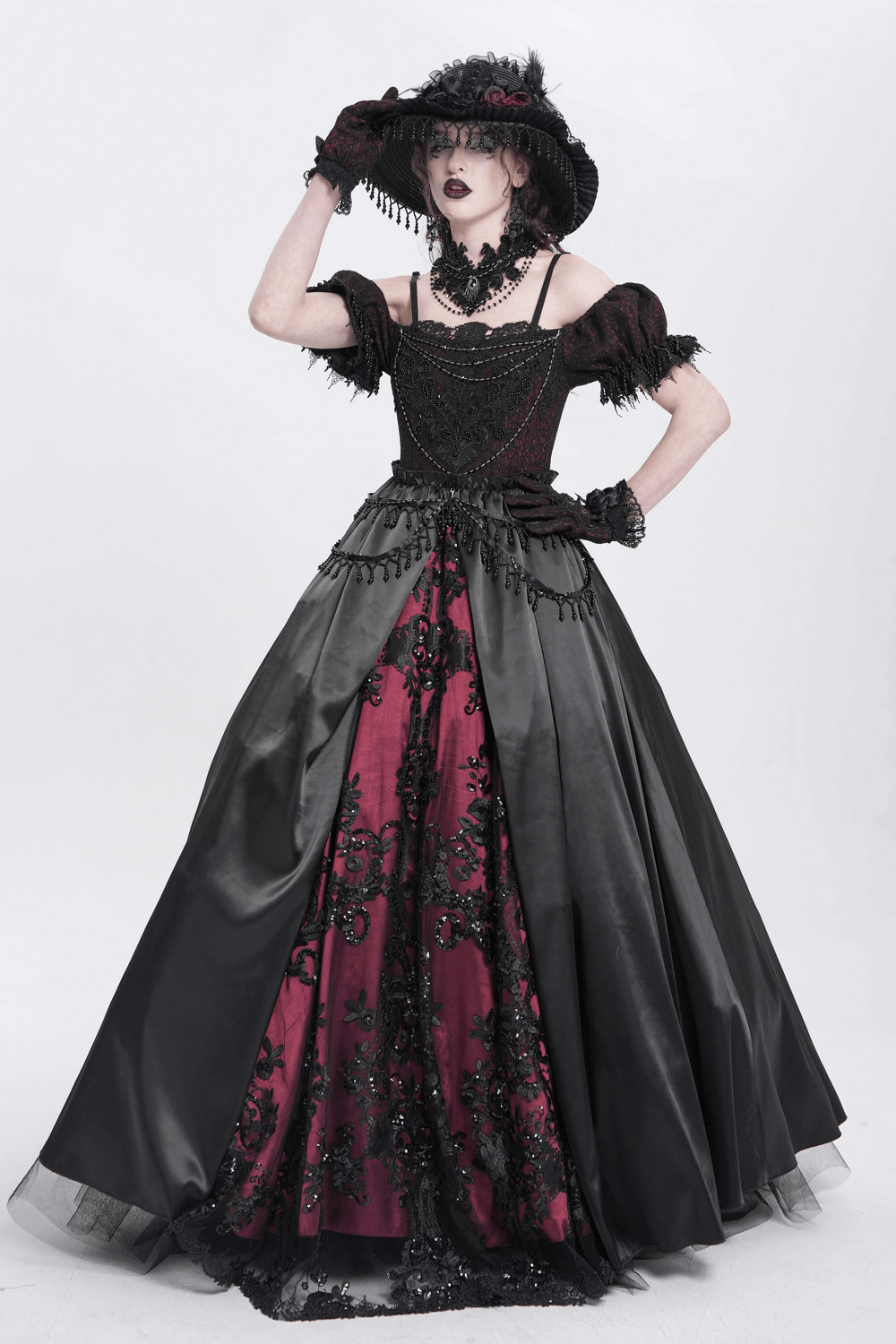 Elegant model in a gothic black and red Victorian dress with intricate lace and feathered hat, embodying dark elegance.