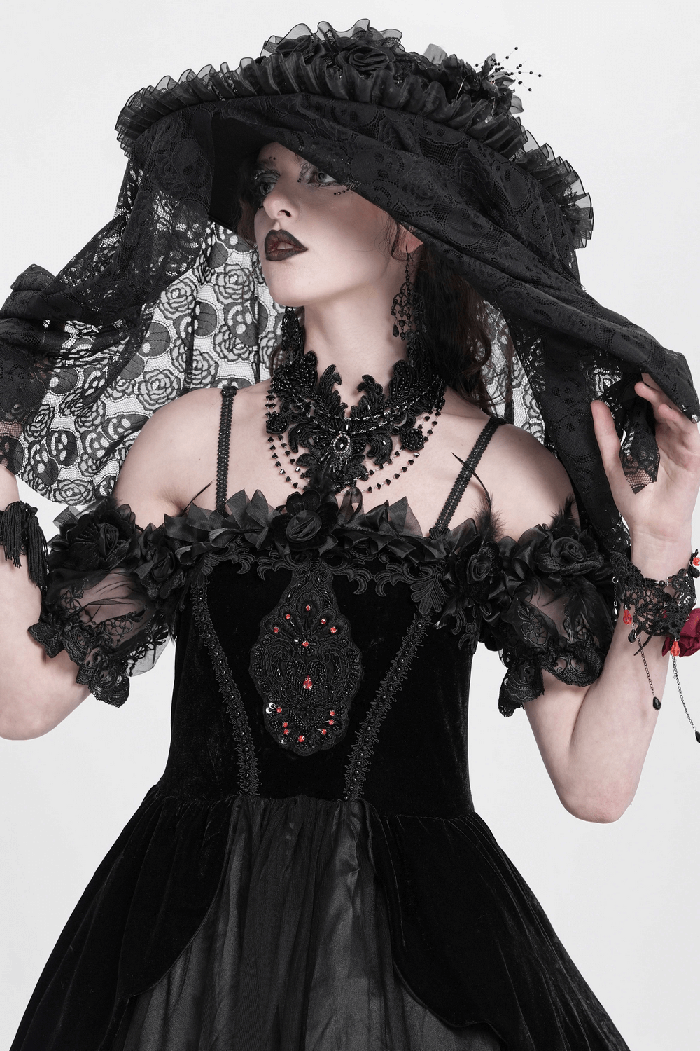 Model in a gothic black dress, wearing a lace choker necklace and broad-brimmed hat, embodying dark elegance.