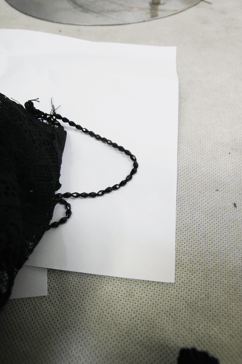 Close-up of intricate black lace fabric with a delicate chain detail on a light background.