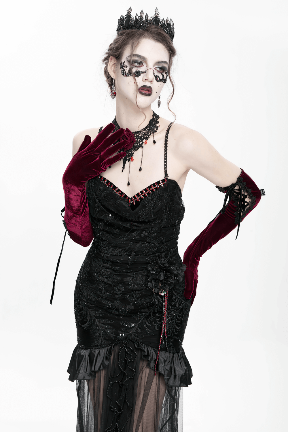 Gothic model in black velvet and sheer mesh dress with red gloves and crown, exuding dark elegance and romance.