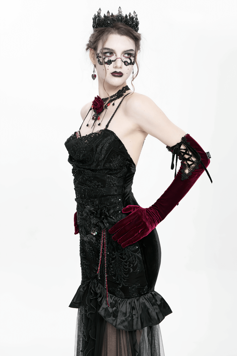 Elegant model in a gothic black velvet dress with sheer mesh, accessorized with gloves and a crown, showcasing dark romance.